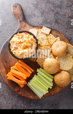 Pimento Cheese ist ein vielseitiges, cremiges Dip, das mit Gemüse und Crackern auf dem Holzbrett auf dem Tisch serviert wird. Vertikale Draufsicht von oben Stockfoto