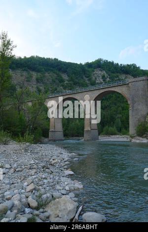 Bögen des alten Acquedukts über dem Fluss Enza in Neviano degli Arduini, Parma, Emilia Romagna, Italien über die Berge und den Himmel Stockfoto