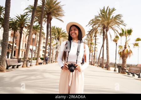 Junge lateinamerikanische Touristin, die ihre Strandreise in Spanien mit der Kamera festhält. Stockfoto