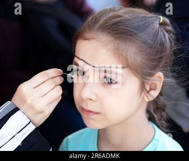 Die Hand des Künstlers malt auf das Gesicht eines kleinen Mädchens. Kinderurlaub. Stockfoto