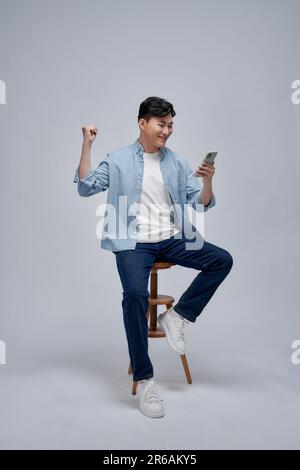 Ein junger asiatischer Mann spielt mit einer App für Mobiltelefone und hebt den Arm hoch, um den Erfolg zu feiern Stockfoto