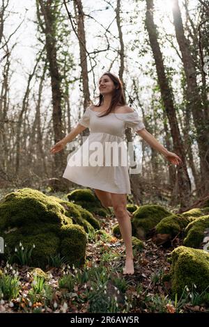 Schneeglöckchen galanthus-Frau. Sie steht in einem weißen Kleid auf einer Wiese mit Schneeglöckchen in einem Frühlingswald Stockfoto