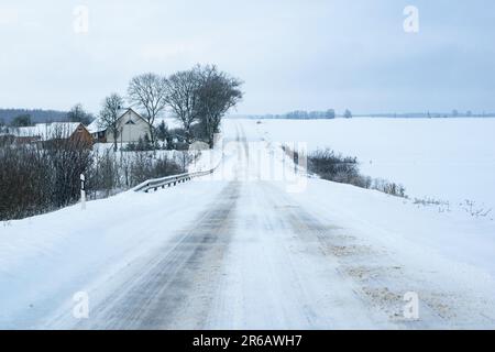 Eine ruhige Winterszene mit einer Landstraße mit schneebedeckten Bäumen und mehreren gemütlichen Häusern im Hintergrund Stockfoto