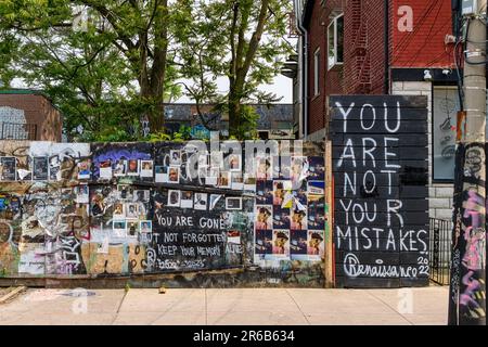 Toronto, Kanada - 4. Juni 2023: Kensington Market. Eine Fotoplatine mit einer Nachricht. Gebäude und Bäume bilden die Kulisse. Stockfoto