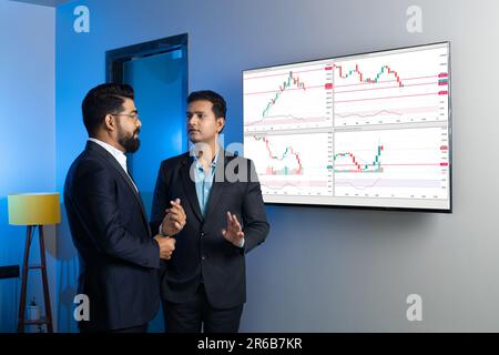 Indische Geschäftsleute, die online im Büro über Aktien handeln und diskutieren. Börsenmakler, die Indizes auf dem großen Computerbildschirm ansehen. Krypto A Stockfoto