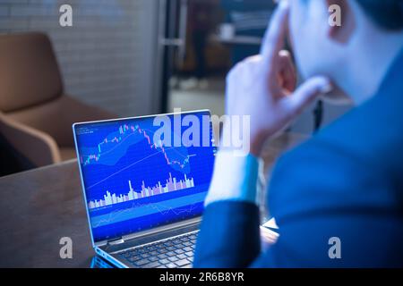 Stress Geschäftsmann oder Börsenhändler schaut auf den Laptop-Bildschirm und zeigt Kerzenleuchter-Diagrammgrafik geht nach unten, Finanzmarkt-Crash. Handelsverluste, Stockfoto