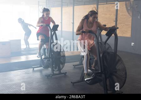 Die ganze Länge von Frauen verschiedener Rassen, die im Fitnessstudio auf Crosstrainer trainieren, Kopierraum Stockfoto