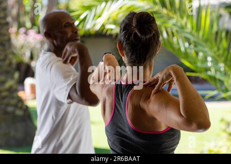 Fokussierter, vielseitiger Senior-Mann, der in Pilates-Klasse mit einer Trainerin trainiert Stockfoto