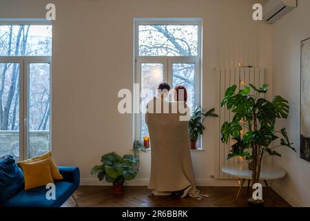 Familienpaar, Frau, Ehemann, der sich umarmte und das Fenster sah, das im Wohnzimmer zu Hause stand. Stockfoto