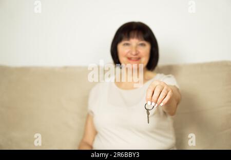 Porträt einer attraktiven, fröhlichen Frau mittleren Alters, die einen Schlüssel ihres neuen Hauses in der Hand hält. Stockfoto