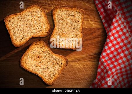 Nahaufnahme von drei Zwiebeln auf einem alten Holztisch mit einer rot-weiß karierten Tischdecke. Stockfoto