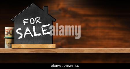 Schild Für Den Verkauf Von Immobilien. Tafel in Form eines Hauses mit Text zum Verkauf und einer Rolle Euro-Banknoten auf einem Holztisch mit Kopierbereich. Stockfoto