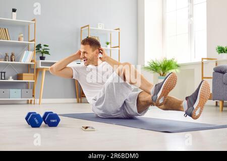 Ein attraktiver, sportlicher junger Mann im weißen T-Shirt, der Sport macht und zu Hause die Presse schüttelt. Stockfoto