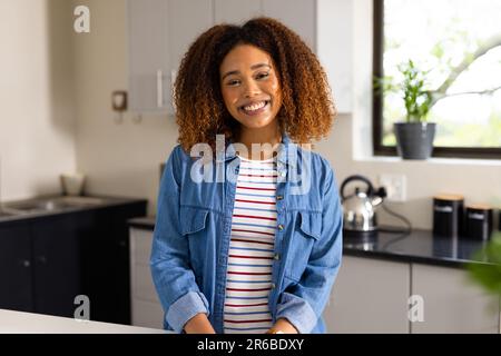 Porträt einer glücklichen, birassischen Frau mit lockigem, lächelndem Haar in der Küche Stockfoto