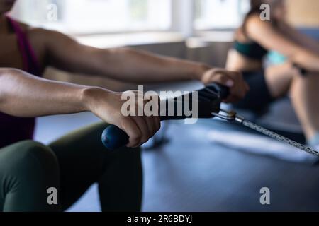 Gekürzte Hände einer birassischen jungen Frau, die den Griff einer Rudermaschine im Fitnessclub zieht, Kopierraum Stockfoto