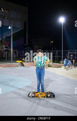 San Salvador, San Salvador, El Salvador - 11. November 2022: Brown Girl Child steht glücklich mit den Füßen unter einem Skateboard in Blue Shirt und Jeans Stockfoto