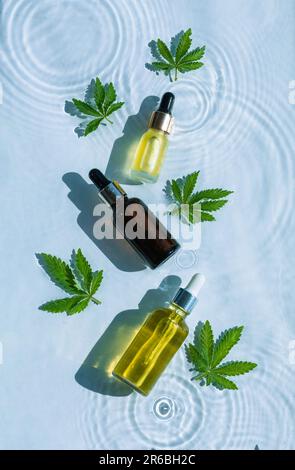 CBD-Ölflaschen, blauer Wasserhintergrund mit Tropfen, Wellen und Blättern aus Hanf, Marihuana. Flach liegend, Draufsicht. Stockfoto