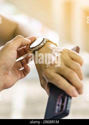 Nahaufnahme eines Mannes mit dem Daumenfinger, der der Frau beibringt, wie die Anwendung auf einer Smartwatch verwendet wird. Ein Mann bringt einer Frau vor, wie man eine Smartwatch benutzt Stockfoto