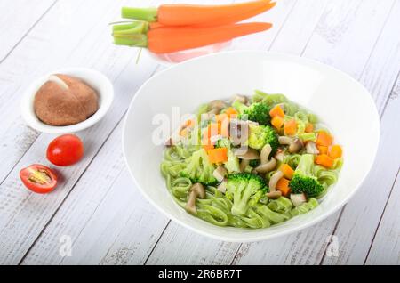 Eine Schüssel gefüllt mit Pasta und Gemüse auf einem Holztisch. Stockfoto