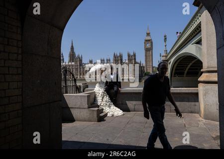 Chinesische frisch Verheiratete, sitzen Sie entlang der Mauer am Ufer der Themse mit Blick auf die Houses of Parliament, während Sie ein Foto an einem schlechten Sommertag in Großbritannien machen. Stockfoto