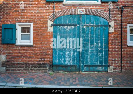 Vorderansicht einer alten Ziegelfassade mit geschlossenem Tor und kleinen Fenstern auf beiden Seiten. Stockfoto