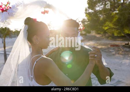 Romantisches junges Paar aus Kaukasiern, das bei der Hochzeitszeremonie bei Sonnenuntergang am Strand tanzt Stockfoto