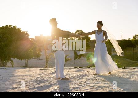 Frisch verheiratetes, weißes junges Paar tanzt am Sandstrand vor klarem Himmel bei Sonnenuntergang, Kopierraum Stockfoto