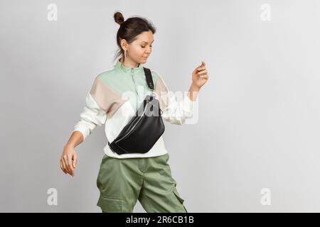 Frau trägt Crossbody eine schwarze Ledergürteltasche mit grauem Hintergrund. Handgefertigtes Leder Accessoires Stockfoto