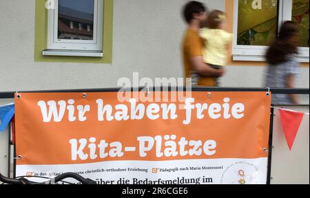 Leipzig, Deutschland. 08. Juni 2023. Eine Frau und ein Mann mit einem Kind in den Armen gehen an einem neuen Kindergarten vorbei, wo kostenlose Kindergartenplätze auf einem Poster beworben werden. Die Einrichtung ist der erste Kindergarten in Deutschland mit rumänischen Wurzeln und stellt ein Pilotprojekt dar, dem weitere Kindergärten in Deutschland folgen werden. Kredit: Waltraud Grubitzsch/dpa/Alamy Live News Stockfoto