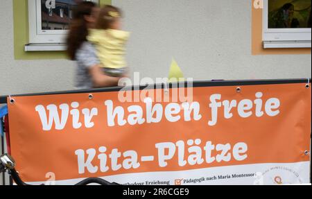 Leipzig, Deutschland. 08. Juni 2023. Eine Frau mit einem Kind in ihren Armen geht an einem neuen Kindergarten vorbei, wo kostenlose Kindergartenplätze auf einem Poster beworben werden. Die Einrichtung ist der erste Kindergarten in Deutschland mit rumänischen Wurzeln und stellt ein Pilotprojekt dar, an das sich weitere Kindergärten in Deutschland anschließen werden. Kredit: Waltraud Grubitzsch/dpa/Alamy Live News Stockfoto