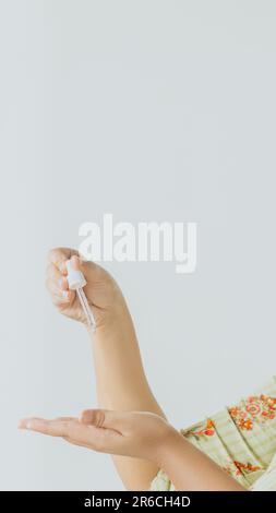 Eine junge Frau, die eine Feuchtigkeitscreme für das Gesicht mit einer Pipette aufträgt Stockfoto