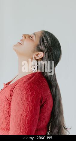 Eine junge Erwachsene Frau mit rotem Haar steht in einer urbanen Umgebung und trägt einen leuchtend roten Pullover Stockfoto