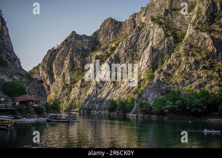 Foto im Canyon Matka in der Nähe der Stadt Skopje in Mazedonien mit felsigen Hügeln/Bergen, Booten und Reflexionen der Natur auf dem See. Stockfoto