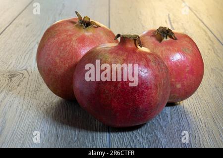 Drei frische reife Granatäpfel auf einem grauen Holztisch. Nahaufnahme Stockfoto