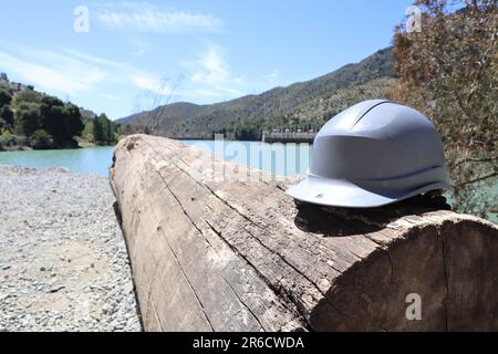 Grauer Helm auf einem Baumstamm in der Nähe einer Flusslandschaft, Wasserkraftwerk, Tajo de la Encantada Reservoir, caminito del rey, Malaga, Spanien Stockfoto