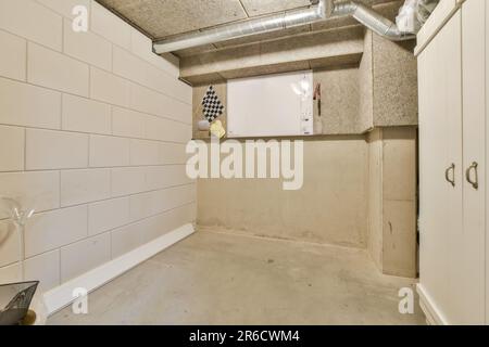 Ein unvollendeter Untergeschossbereich mit weißen Wänden und grauen Bodenfliesen an der Wand, es gibt einen Wasserkocher im Raum Stockfoto