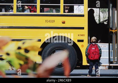 Ein Grundschüler trägt einen großen Rucksack und bereitet sich vor, an seinem ersten Schultag in einen Schulbus zu steigen Stockfoto