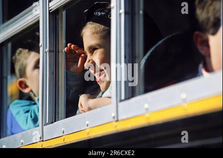 Ein Kasian-Schüler, der aus dem Fenster eines Schulbusses guckt und sich verabschiedet Stockfoto