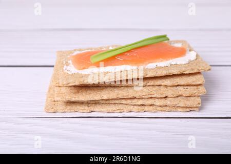 Leckeres Knusperbrot mit Lachs, Frischkäse und grünen Zwiebeln auf weißem Holztisch, Nahaufnahme Stockfoto