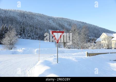 Verkehrsschild in der Nähe der mit Schnee bedeckten Straße am Wintertag Stockfoto