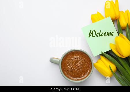 Willkommenskarte, wunderschöne gelbe Tulpen und eine Tasse aromatischen Kaffees auf weißem Hintergrund, flach liegend Stockfoto