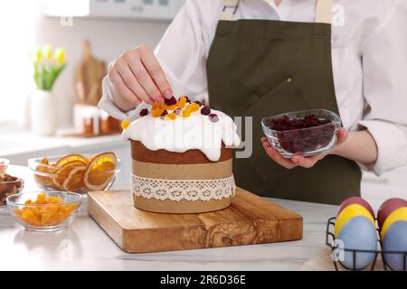 Frau dekoriert köstlichen Osterkuchen mit getrockneten Preiselbeeren an einem weißen Marmortisch in der Küche, Nahaufnahme Stockfoto