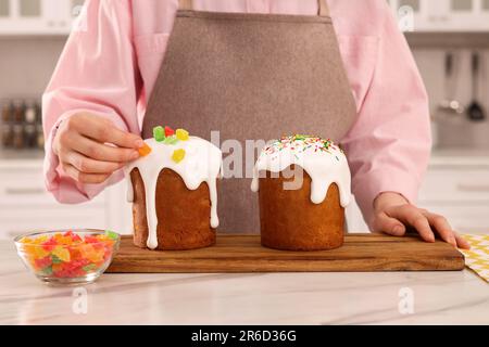 Eine Frau, die köstlichen Osterkuchen mit kandierten Früchten dekoriert, an einem weißen Marmortisch in der Küche, Nahaufnahme Stockfoto