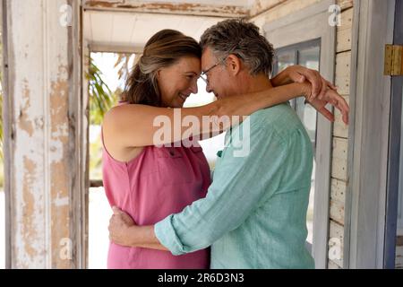 Seitlicher Blick auf ein weißes Seniorenpaar, das sich umarmt und sich anschaut, während man auf dem Balkon steht Stockfoto