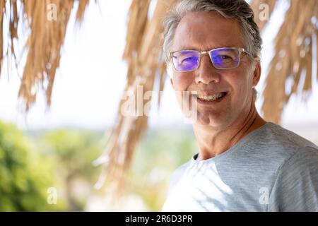 Porträt eines weißlichen lächelnden Seniorenmannes mit Brille, der im Sommer im Touristenresort steht Stockfoto
