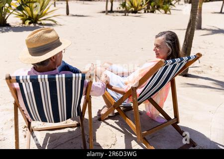 Romantisches weißes Seniorenpaar, das Händchen hält und auf Liegestühlen am Sandstrand sitzt, Kopierbereich Stockfoto