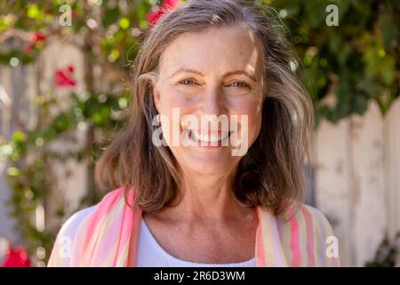 Nahaufnahme von einer schönen weissen Seniorin, die vor der Kamera lächelt, gegen Pflanzen, Kopierraum Stockfoto