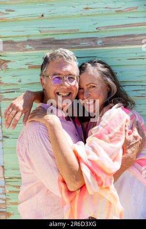 Portrait eines lächelnden weißlichen Seniorenpaares, das sich umarmt und an einer Holzwand steht Stockfoto