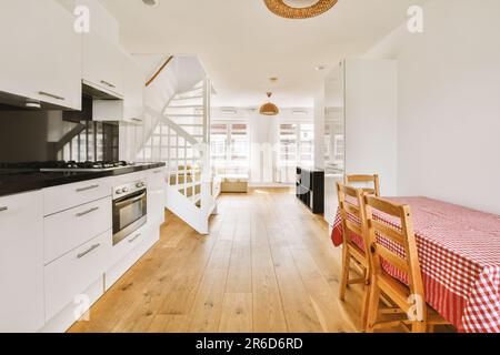 Ein Küchen- und Essbereich in einem Haus mit weißen Wänden, Holzfußboden und einer offenen Treppe, die in die zweite Etage führt Stockfoto