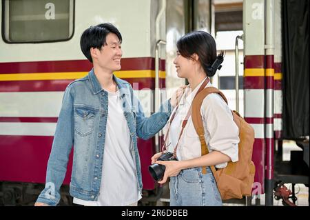 Ein hübsches, junges asiatisches Touristenpaar spricht gerne auf dem Bahnsteig, bevor es in den Zug steigt. Sommerferienkonzept Stockfoto